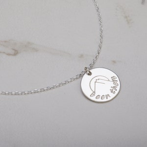 May include: A silver necklace with a round pendant that has a mountain range silhouette and the text "been there" engraved on it.