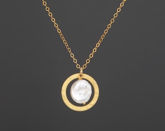 May include: A gold-toned necklace featuring a delicate chain and a circular pendant with a hammered texture. Suspended within the center of the gold circle is a single, irregular, white freshwater pearl, attached by a small gold-toned jump ring.