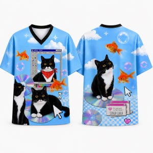 Puede incluir: Una camiseta azul claro con cuello en V que presenta un estampado gráfico de gatos blancos y negros, peces dorados, discos compactos y elementos de interfaz informática, incluyendo una ventana de programa de pintura y un cuadro de texto Do you want to be friends.