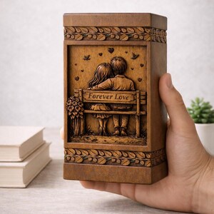 Puede incluir: Caja de madera marr&oacute;n con un relieve tallado que representa a una pareja en un banco con la inscripci&oacute;n "Forever Love". La caja tiene patrones de hojas decorativas y peque&ntilde;os detalles de corazones y p&aacute;jaros. Tambi&eacute;n se ve un ramo de flores talladas.