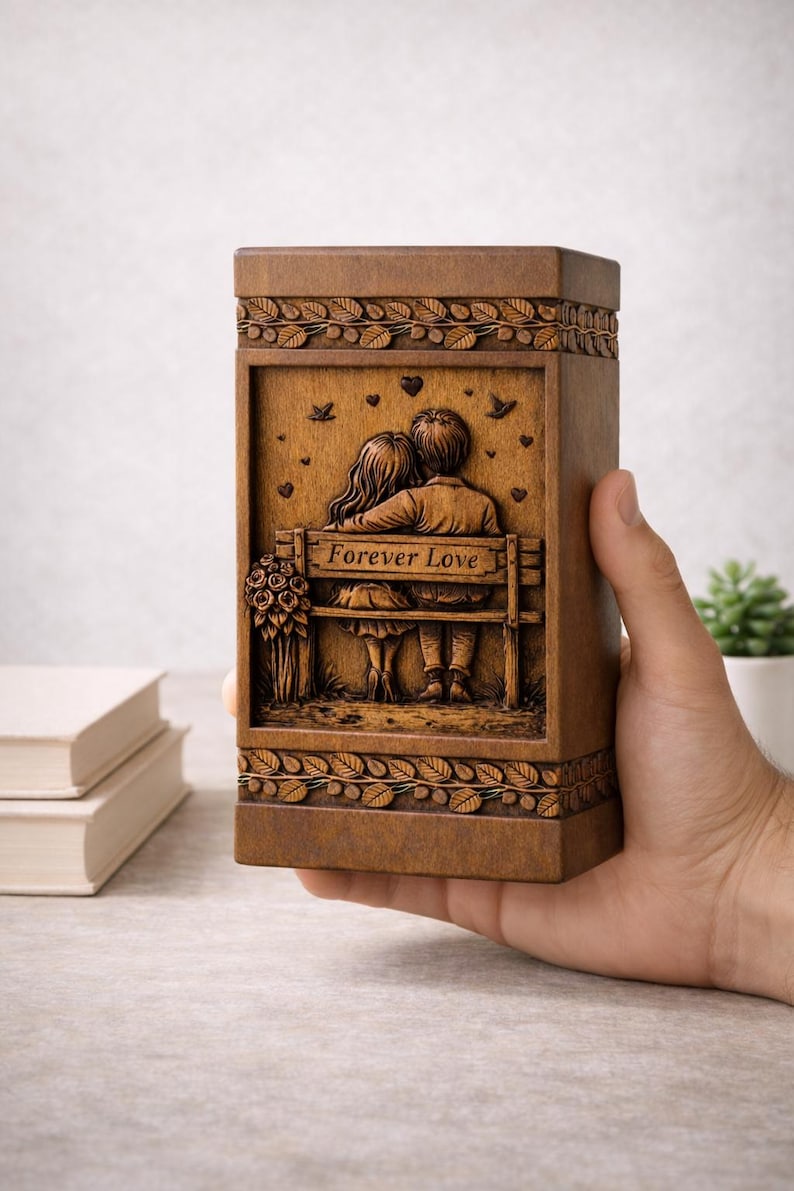 Puede incluir: Caja de madera marr&oacute;n con un relieve tallado que representa a una pareja en un banco con la inscripci&oacute;n "Forever Love". La caja tiene patrones de hojas decorativas y peque&ntilde;os detalles de corazones y p&aacute;jaros. Tambi&eacute;n se ve un ramo de flores talladas.