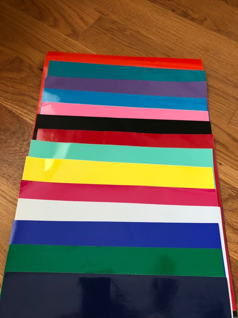 May include: A stack of colorful vinyl sheets in various shades, including red, teal, purple, blue, pink, black, red, mint green, yellow, magenta, white, and navy. The sheets are arranged in a neat, organized pile.