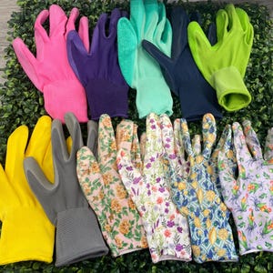 May include: A collection of gardening gloves in various colors and patterns. Includes pink, purple, green, yellow, gray, and floral designs. The gloves are arranged on a bed of green foliage.