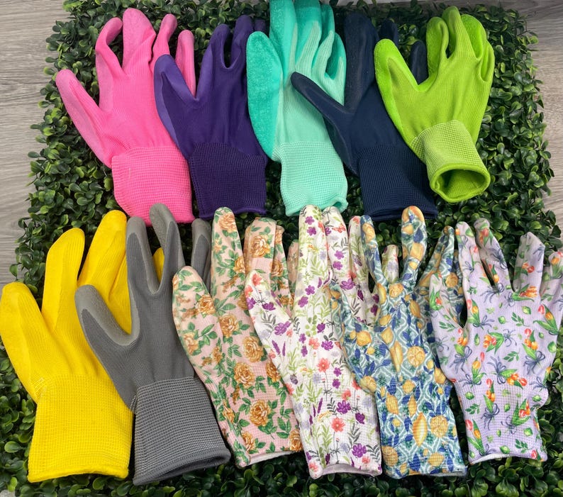 May include: A collection of gardening gloves in various colors and patterns. Includes pink, purple, green, yellow, gray, and floral designs. The gloves are arranged on a bed of green foliage.