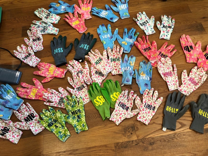 May include: A collection of gardening gloves in various colors and patterns, including floral and polka dot designs. Many gloves are personalized with names like "Jess," "Suzie," and "Linda." Some gloves are solid colors, such as green and gray.