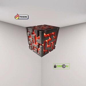 Puede incluir: Lámpara cúbica geométrica con diseño de laberinto. La lámpara es de color gris oscuro con un brillo rojo en su interior. La palabra "TRENDING" aparece en una pancarta en la esquina superior izquierda.