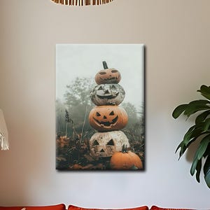 May include: A rectangular wall art print featuring a vertical stack of four carved orange pumpkins with carved faces, set in a foggy outdoor landscape with trees and fallen leaves. The print is displayed on a plain wall above a bright orange sofa.