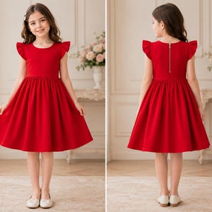 May include: A vibrant red dress with a round neckline and flutter sleeves. The dress features a fitted bodice and a flared skirt. A gold zipper runs down the back. The girl is wearing white shoes. The dress is suitable for special occasions.