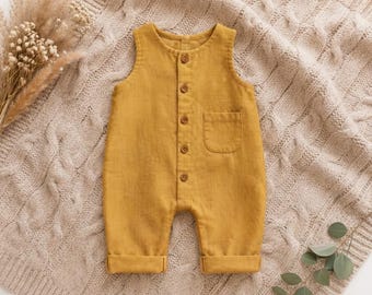 May include: A sleeveless mustard yellow romper featuring a round neckline, a front button placket with five small brown buttons, and a single patch pocket on the chest. The garment has cuffed leg openings and a simple, straight-leg silhouette.