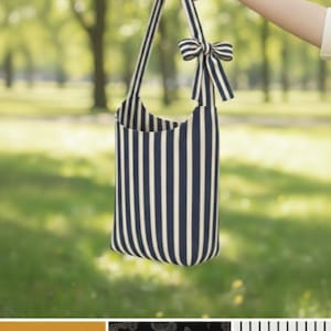 May include: A DIY Hobe bag sewing pattern. The bag is navy blue and white striped with matching straps and a bow. The bag is held up by a hand against a blurred green background. The text "DIY HOBE BAG SEWING PATTERN" and "INSTANT DOWNLOAD PDF" is at the top.