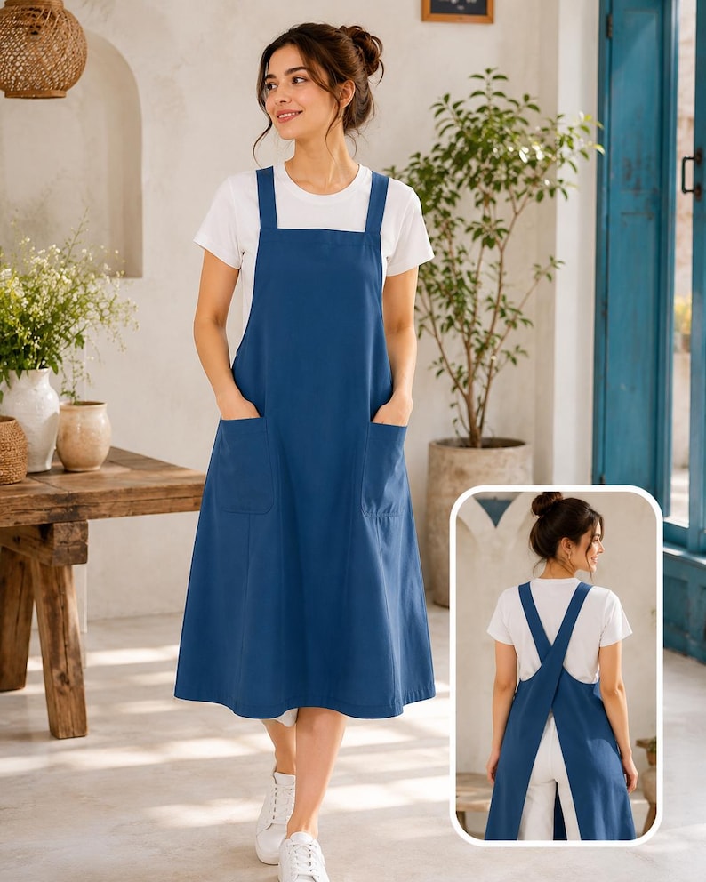 May include: A solid blue pinafore dress featuring a square neckline, wide shoulder straps, and two large front patch pockets. The garment is worn over a plain white short-sleeved t-shirt. An inset shows the back with a crisscross strap design.
