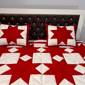 May include: A bed featuring a dark brown tufted headboard with embedded crystals, two square pillows with a red star pattern on a white background, and a matching quilt displaying a repeating red and white star geometric design.