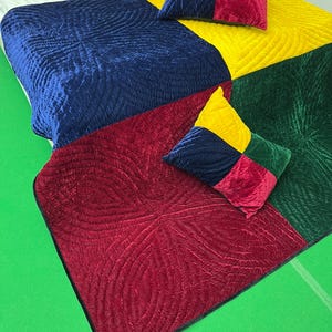 May include: A colorful quilt and two matching pillows. The quilt is divided into sections of blue, yellow, green, and red. The pillows have a patchwork design with the same colors. The quilt has a quilted pattern.