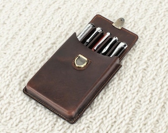 May include: A dark brown leather pen case with a flap closure and a brass-toned metal stud fastener. The case contains four pens with silver-toned clips and caps. The leather has visible stitching along the edges and a smooth, matte finish.