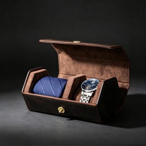 May include: A dark brown leather watch and accessory roll with a soft brown interior lining. The case features a brass snap closure and holds a blue textured necktie on the left side and a silver-tone analog wristwatch with a blue face on the right.