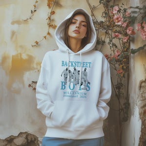 Könnte beinhalten: Weißer Kapuzenpullover mit dem Schriftzug "BACKSTREET BOYS" in Hellblau und einer Grafik der Bandmitglieder. Der Hoodie enthält auch "INTO THE MILLENNIUM Düsseldorf 2026". Er hat eine Kapuze mit Kordelzug und eine Vordertasche.