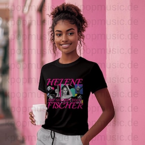 Op de afbeelding: Zwart T-shirt met een roze afbeelding van Helene Fischer en de tekst "HELENE FISCHER 360° STADIUM TOUR". Het shirt heeft een ronde hals en korte mouwen. Een vrouw houdt een witte beker vast.