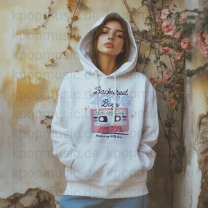 Puede incluir: Sudadera con capucha blanca con el texto "Backstreet Boys 2026" y un gráfico de cinta de cassette. El diseño incluye las frases "Into the Millennium" y "oussefore" en un estilo retro. La sudadera tiene una capucha con cordón.