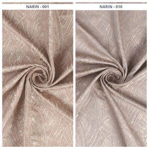 May include: Two swatches of fabric, one in a light taupe color and the other in a light grey color. Both fabrics have a textured, shimmering pattern with a feathery design. The fabric is gathered and swirled, showing the texture and sheen.