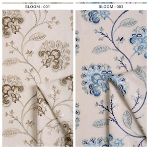 May include: Two fabric samples with floral embroidery. One features beige and brown flowers with the text "BLOOM - 001". The other has blue flowers and the text "BLOOM - 003". Both are on a cream-colored background.