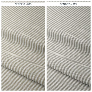 Puede incluir: Dos muestras de tela con un patrón de rayas. La muestra de la izquierda es beige y blanca, etiquetada como "SENECIO - 003". La muestra de la derecha es gris y blanca, etiquetada como "SENECIO - 019". La tela está doblada, mostrando la textura y el tejido.