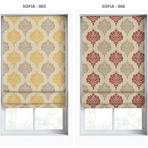 May include: Two Roman shades with a repeating floral pattern. One shade features a cream background with yellow and taupe floral designs. The other shade has a cream background with red and taupe floral designs. Both are mounted inside a white window frame.