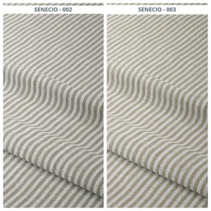 Puede incluir: Dos muestras de tela con un patrón de rayas. La tela tiene rayas alternas de beige claro y blanco. El texto "SENECIO - 002" y "SENECIO - 003" está impreso en la parte superior de cada muestra.