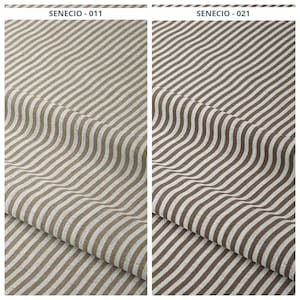 Puede incluir: Dos muestras de tela con un patrón de rayas. La primera muestra, etiquetada como "SENECIO - 011", presenta rayas beige y blancas. La segunda muestra, etiquetada como "SENECIO - 021", tiene rayas marrones y blancas. La tela está doblada, mostrando la textura.