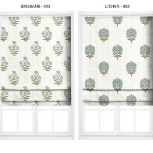 May include: Two Roman shades with floral patterns. The left shade, labeled "BRISBANE - 003", features a repeating pattern of blue and green flowers on a cream background. The right shade, labeled "LICHEN - 003", has a similar design.