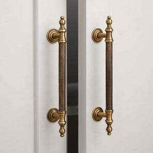 May include: A pair of antique brass door handles. Each handle features a vertical, ribbed design with decorative finials. The handles are mounted on a white door, offering a classic and elegant aesthetic. The handles are made of brass.
