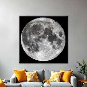 May include: A large, square canvas print of the moon hangs on a gray wall above a gray sofa with orange pillows. The moon is detailed with craters and shadows, set against a black background. The room is decorated with modern furniture and plants.