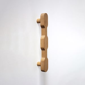 May include: A vertical wooden door pull with a natural finish. The pull has a series of rounded, rectangular shapes connected by a central column. Two cylindrical knobs extend from the top and bottom of the pull.
