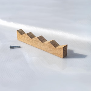 Könnte beinhalten: Ein helles Holzregal mit einem Stufendesign, möglicherweise zum Halten von Gegenständen. Neben dem Regal befindet sich eine kleine Schraube. Das Holz hat eine natürliche Maserung und eine hellbraune Farbe. Das Regal hat vier Stufen.