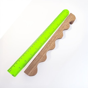 Könnte beinhalten: Ein leuchtend grünes Lineal mit schwarzen Markierungen und einer Holzbasis mit gewelltem Rand. Das Lineal ist in Zentimetern markiert. Die Holzbasis ist hellbraun und hat eine einzigartige, dekorative Form. Die Artikel sind auf weißem Hintergrund abgewinkelt.