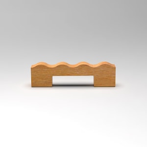 Peut inclure: Un objet en bois brun clair avec un dessus ondulé et une base rectangulaire. L'objet présente deux découpes rectangulaires en bas. Le grain du bois est visible. Il s'agit probablement d'un objet décoratif ou fonctionnel.