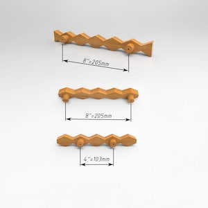 Puede incluir: Tres tiradores de armario de madera marrón claro con un diseño geométrico de múltiples facetas. Dos tiradores presentan una medida entre centros de 205 mm, mientras que el tercer tirador tiene una medida entre centros de 103 mm.