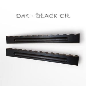 Puede incluir: Dos estantes largos de madera de roble teñida de oscuro con un borde superior ondulado y festoneado y una ranura horizontal central. El texto OAK + BLACK OIL está impreso sobre los estantes en una fuente negra fina con ilustraciones florales.