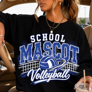 Peut inclure: Un sweat-shirt noir à col rond avec une impression graphique portant le texte SCHOOL MASCOT Volleyball en bleu et blanc. Le motif comprend une illustration de ballon de volley avec un filet en arrière-plan et un effet de mouvement circulaire.