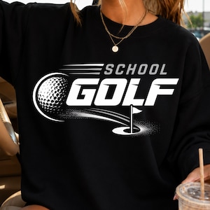 Puede incluir: Una sudadera negra de cuello redondo con un diseño gráfico en blanco que incluye el texto SCHOOL GOLF. El gráfico muestra una pelota de golf en movimiento con líneas de velocidad hacia un hoyo con bandera, todo en un estilo de alto contraste.