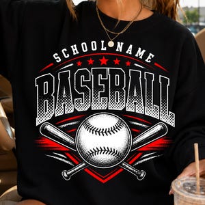 Peut inclure: Un sweat-shirt noir à col rond avec une impression graphique affichant le texte SCHOOL NAME en blanc au-dessus du mot BASEBALL en grande police blanche à effet demi-teinte. Une balle de baseball blanche croise deux battes rouges.