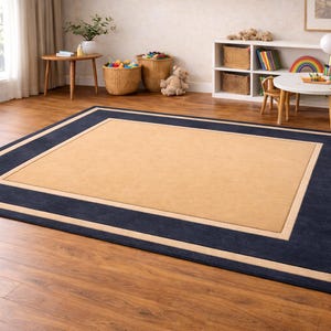 May include: A rectangular area rug with a tan center, bordered by a navy blue frame and a thin beige accent. The rug is placed on a hardwood floor, creating a defined space in a room with natural light.