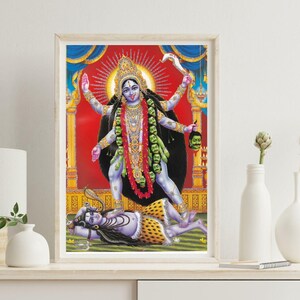May include: Framed print of the Hindu goddess Kali, depicted with multiple arms, standing over a figure. The artwork features vibrant colors, including red, blue, and gold, with intricate details in the figures' attire and surroundings.