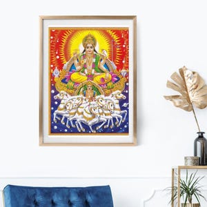 May include: A framed print depicting a Hindu deity seated on a lotus flower, surrounded by a radiant sunburst. The deity is adorned in yellow and green garments, with a halo. Below, seven white horses pull a chariot. The artwork is framed in a light wood.