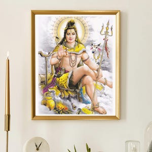 Peut inclure: Une impression encadrée d'une divinité hindoue, représentant une figure avec un châle jaune et des bijoux, assise avec un trident et une vache blanche. L'œuvre est dans un cadre doré, exposée sur une cheminée blanche avec une bougie, une horloge et des objets décoratifs.