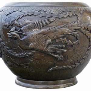 Op de afbeelding: Ronde, bronskleurige decoratieve kom met gedetailleerde reliëfsnijwerk. De kom heeft een ontwerp van een vogel in vlucht met ingewikkelde veren- en bladerpatronen. De kom heeft een brede opening en een stevige basis.