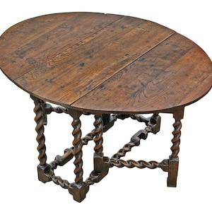 May include: Oval wooden table with a dark brown finish. The tabletop is made of planks and has a hinged design. The legs are intricately carved with a twisted rope design, adding a unique touch to the antique furniture.