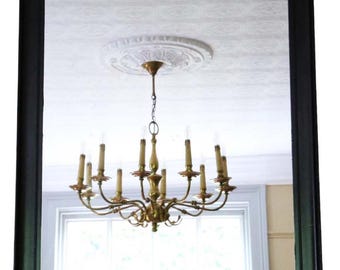 May include: A rectangular mirror with a black frame. The mirror reflects a room with a white ceiling, a chandelier, and a window. The chandelier has multiple candle-shaped lights.