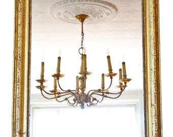 May include: A rectangular antique mirror with a gold-colored, ornate frame. The mirror reflects a chandelier with six candle-shaped lights. The frame has a distressed finish, adding to its vintage appeal. The mirror is a decorative home decor item.