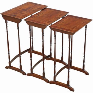 May include: Set of three antique nesting tables. Each table has a rectangular top with a decorative border. The tables are made of dark wood and have slender, turned legs. The largest table is approximately 28 inches long.