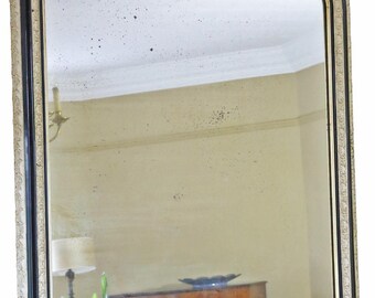 May include: An arched mirror with a black and gold frame. The frame has a decorative, off-white border. The mirror reflects a room with a lamp, a plant, and a wooden cabinet. The mirror's dimensions are not visible.